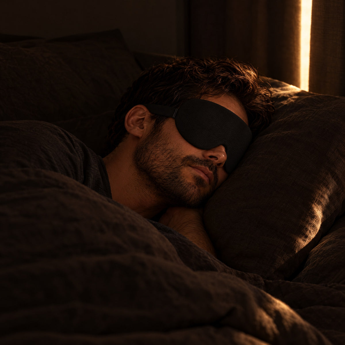 Man sleeping in late in a dark bedroom wearing the black sleep mask